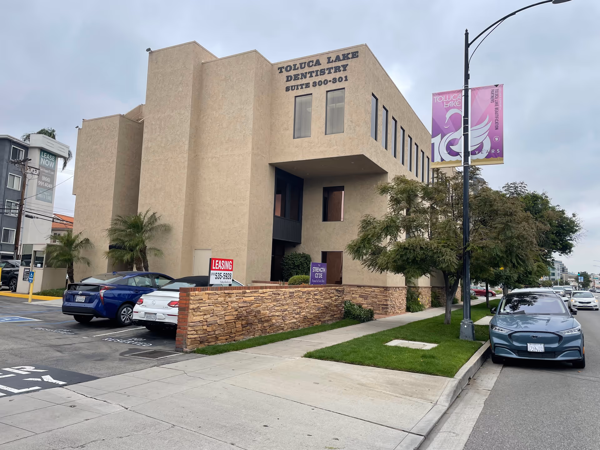 Beige building front labeled Toluca Lake Dentistry with parked cars along the street.
