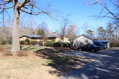 Front view of a single-story senior living facility with parking and trees.