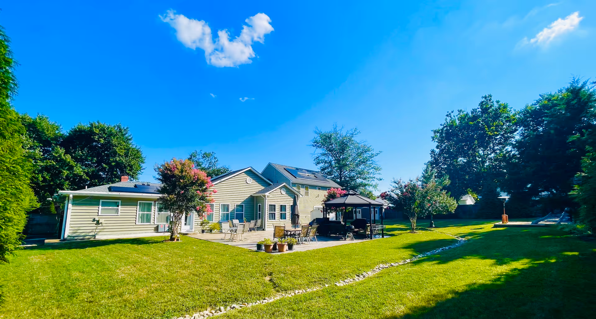 Sunny backyard with a single-story building and patio seating under a gazebo.