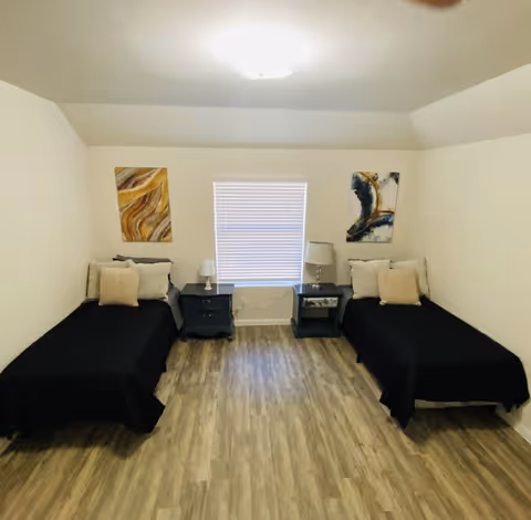 A room with two twin beds, side tables, lamps, and a central window.