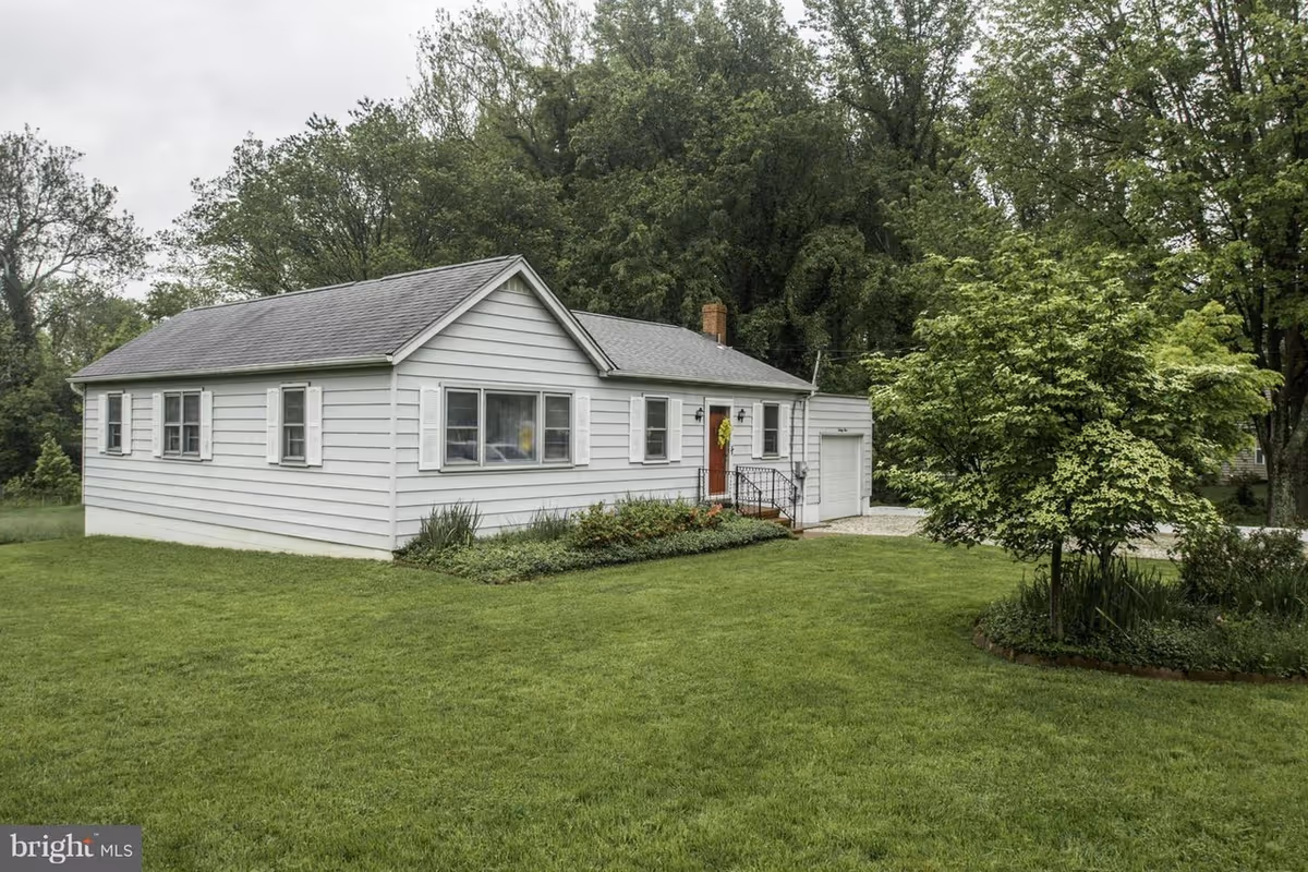 White single-story house with manicured lawn and trees, front entrance visible.