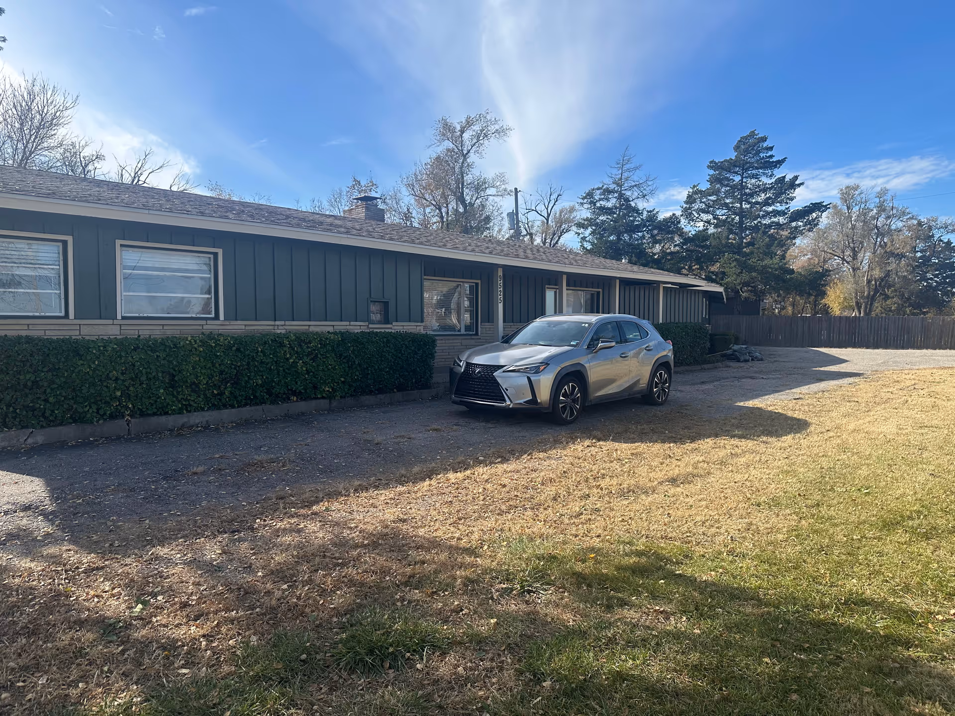 Blue single-story facility exterior with hedge, driveway, and a silver car parked in front.