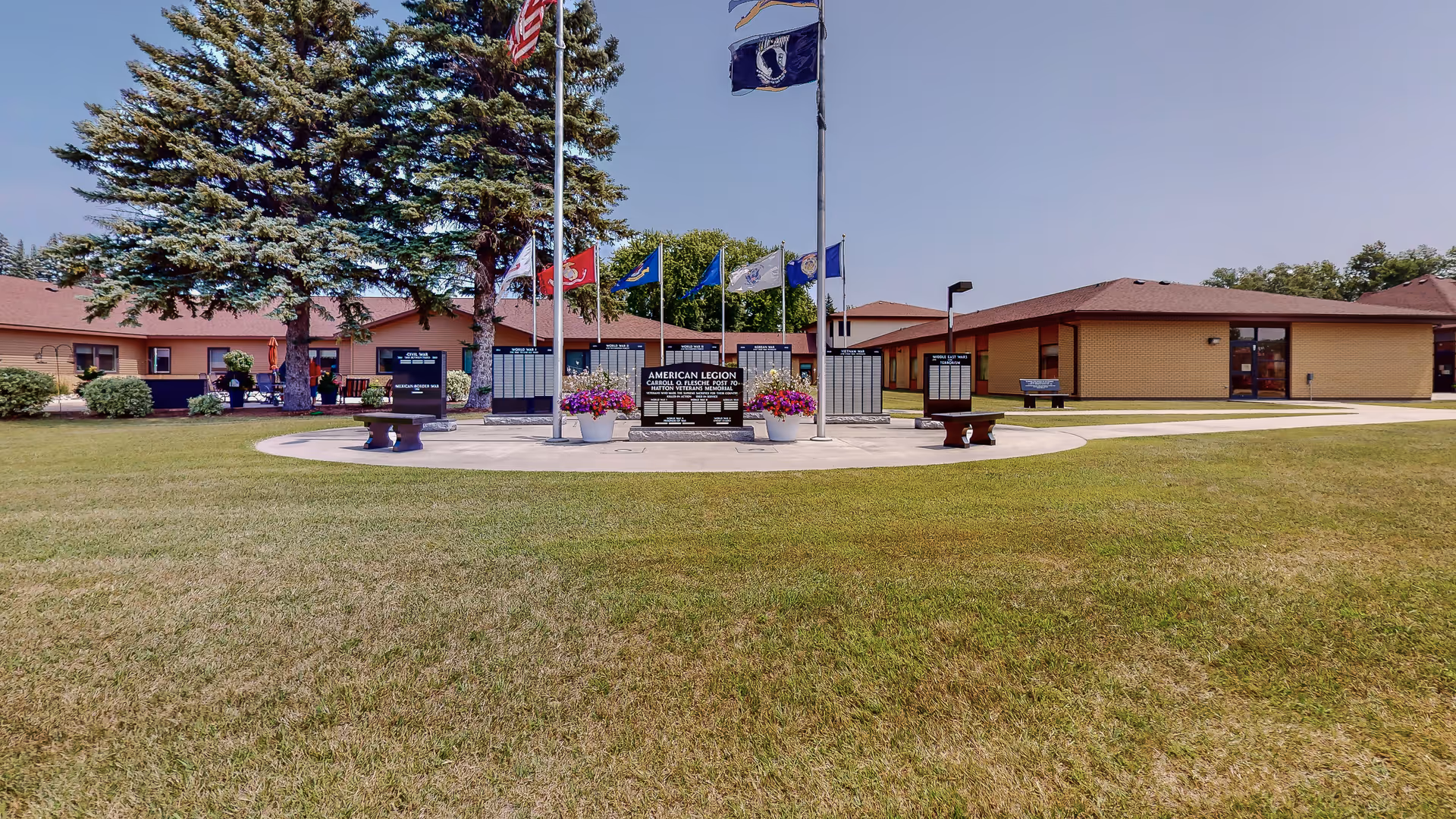 Exterior view of Hatton Prairie Village with circular plaza, flags, benches, and low brick buildings.