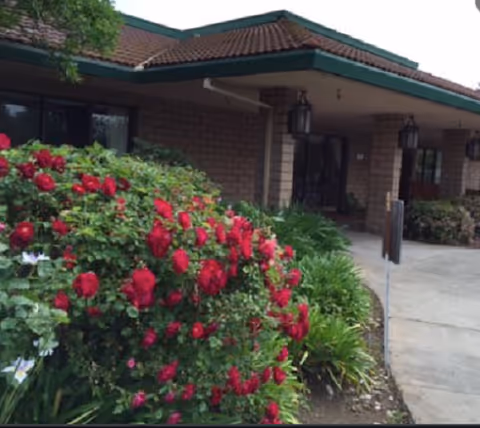 Brick building entrance with a covered porch and vibrant red rose bushes in foreground.