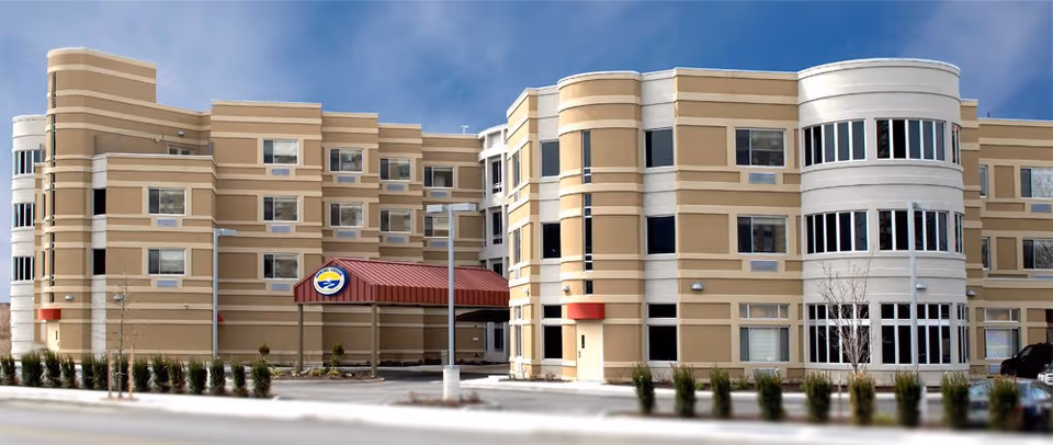Exterior view of a tan multi-story senior care facility with curved white tower.