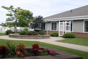 Front exterior of Father Baker Manor senior living facility with a garden bed, walkway, and lawn.