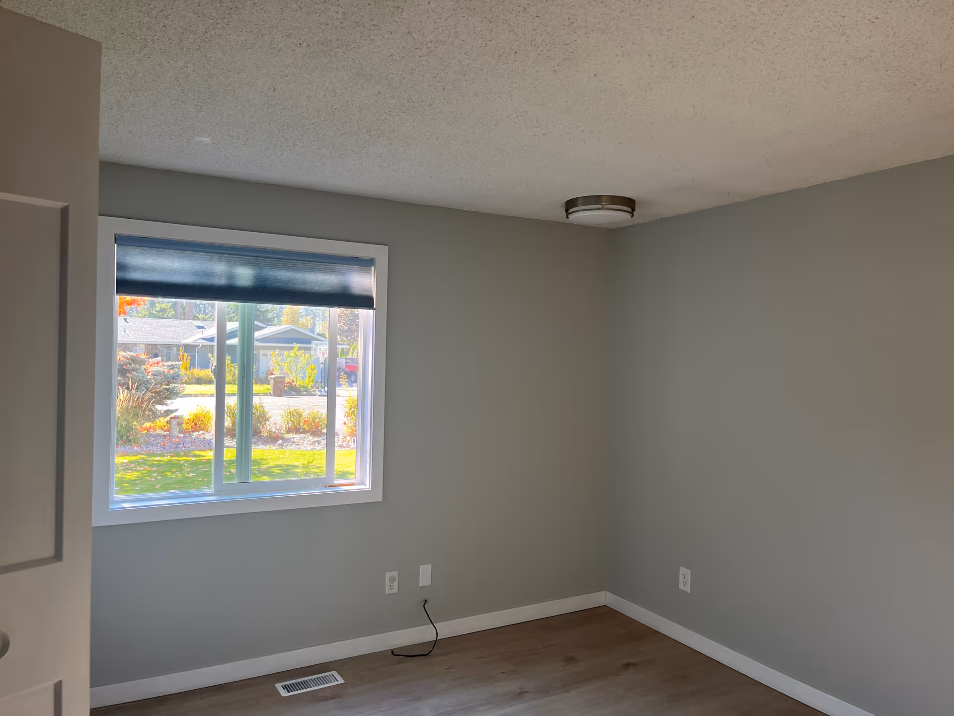 Empty gray room with a window view of yard and street outside.