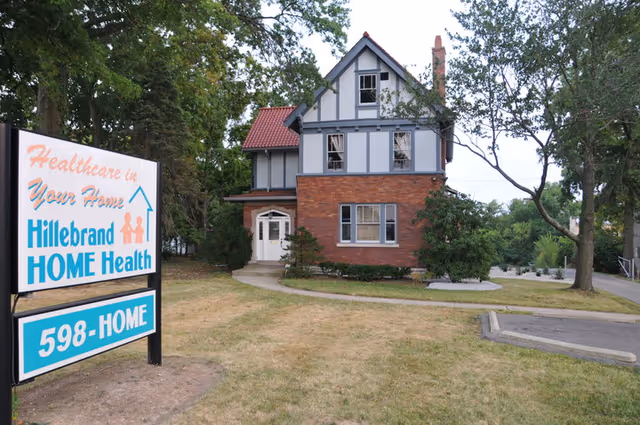 Exterior view of a brick-and-timber two-story senior home with a Hillebrand Home Health sign.