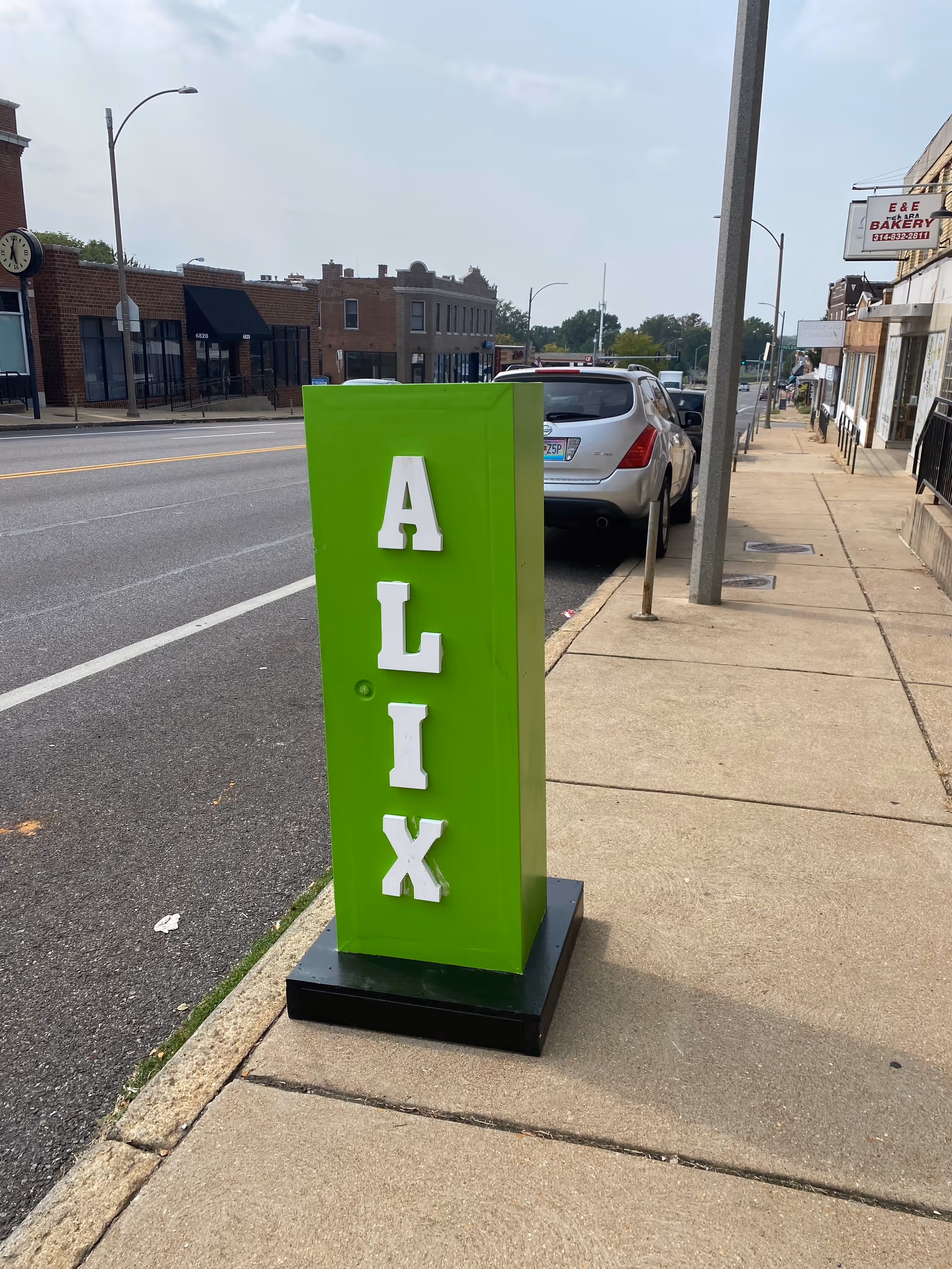 Bright green ALIX sign standing on sidewalk beside a parked car.