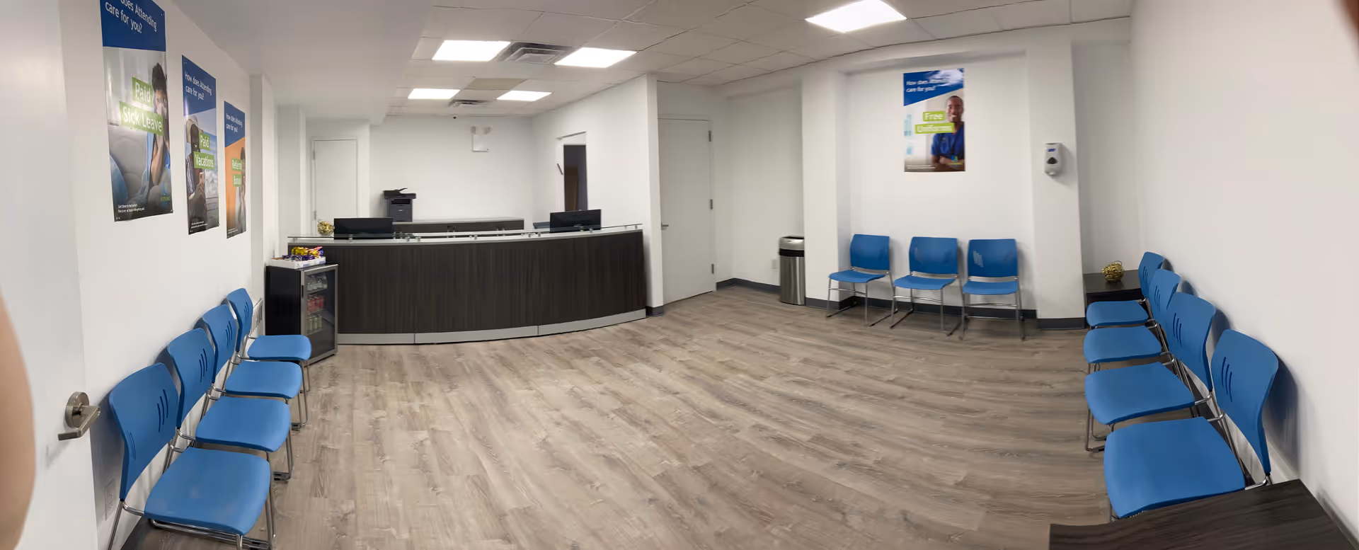 Reception area with blue chairs along walls and a dark curved front desk.