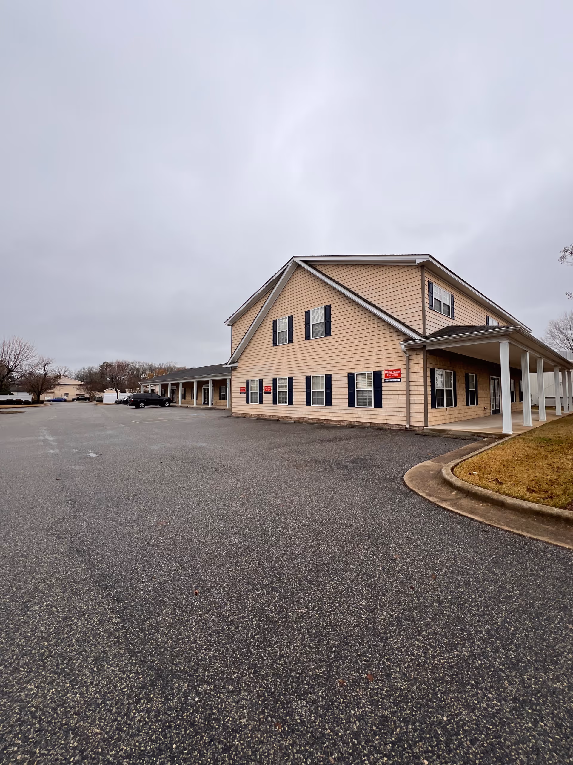 Exterior view of a beige senior home facility with a covered entrance and parking lot.