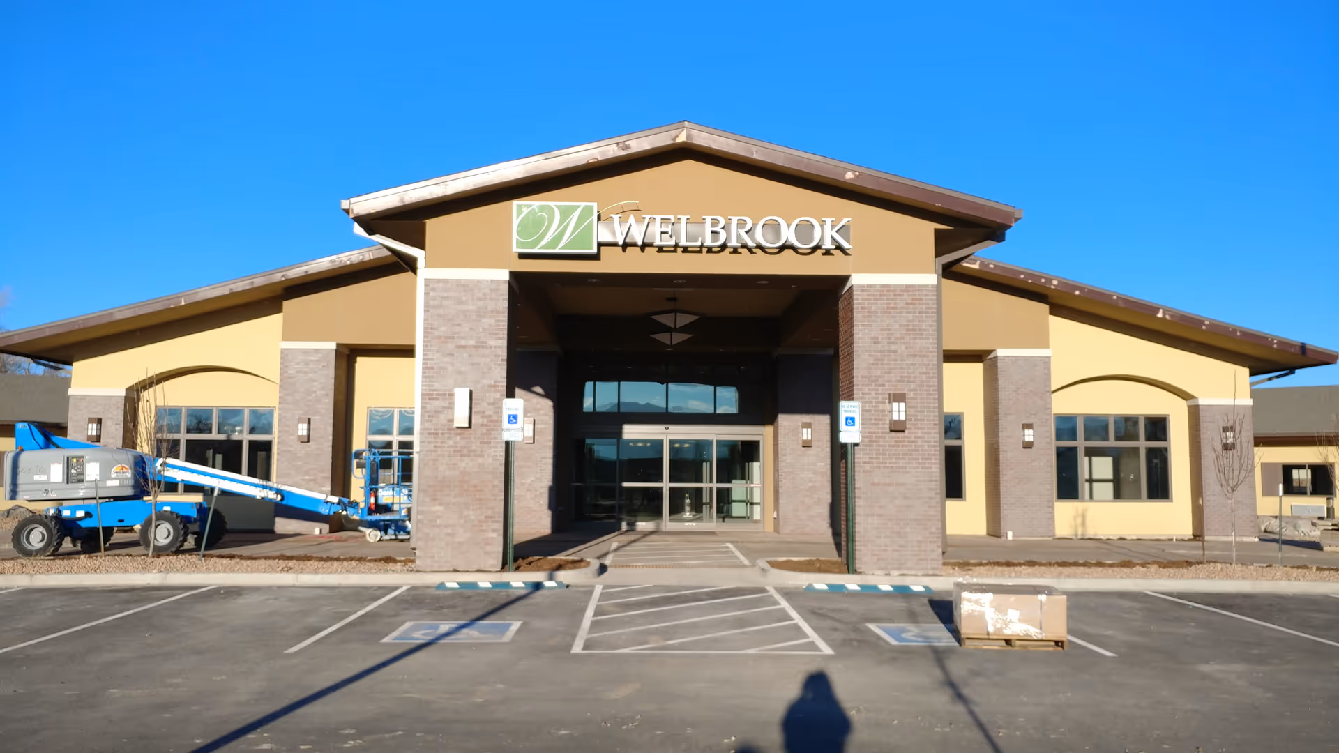 Front view of Welbrook Senior Living building with parking lot and construction equipment.