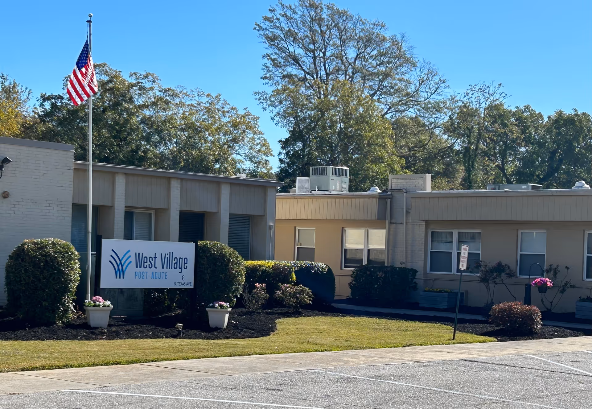 Front exterior of West Village Post-Acute with American flag and sign.