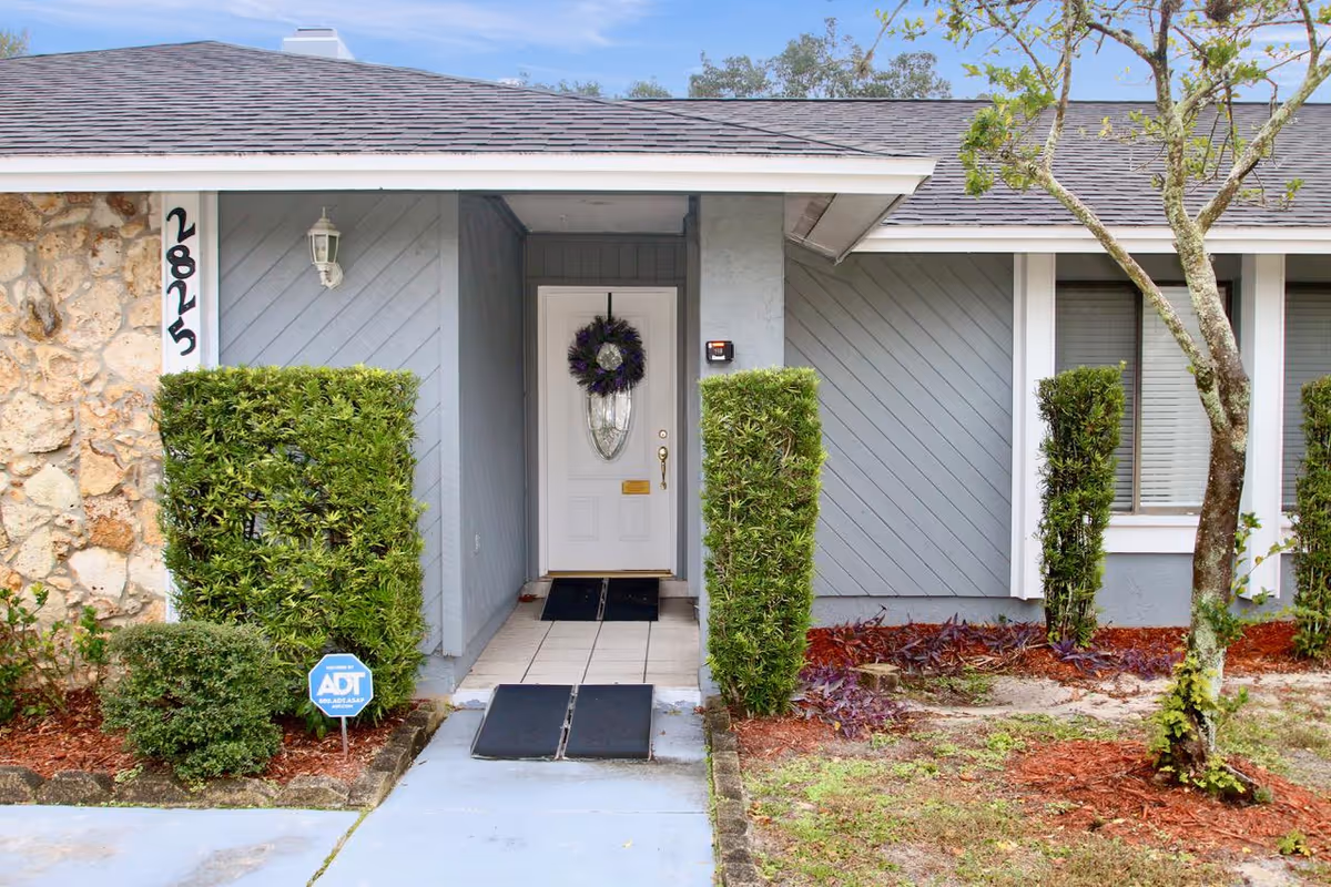 Grey-blue exterior entry with a white door, wreath, and neatly trimmed hedges.