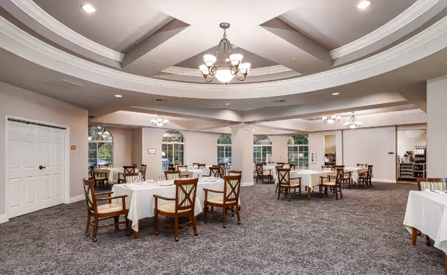 Spacious dining room with round tables, white tablecloths, and chandeliers in Hickory Creek at Hicksville.