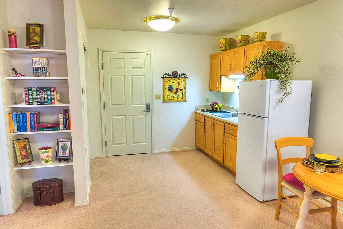 Compact kitchen area with wooden cabinets, a refrigerator, and a small dining table.