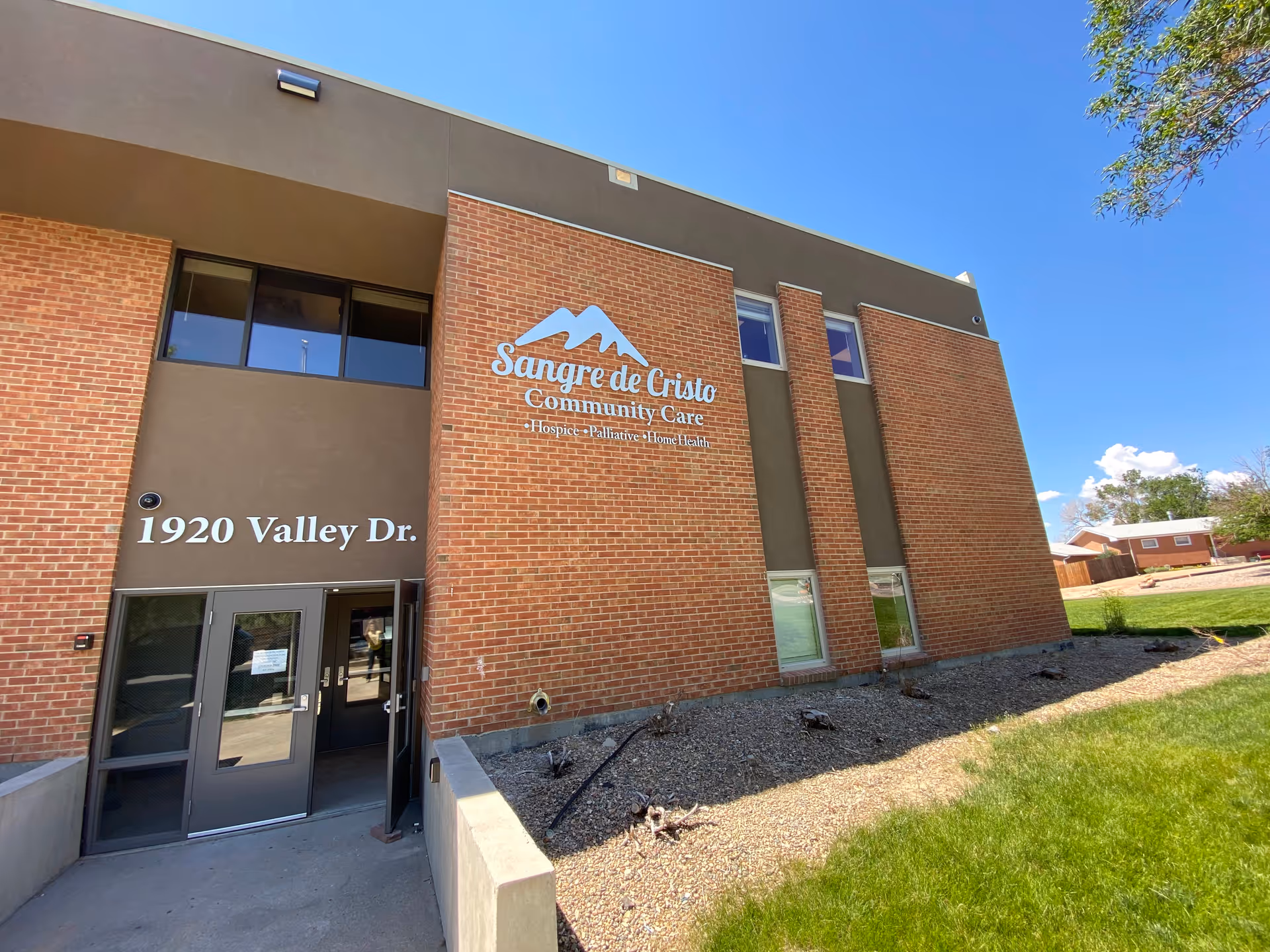 Brick building exterior with glass doors and Sangre de Cristo Community Care sign.