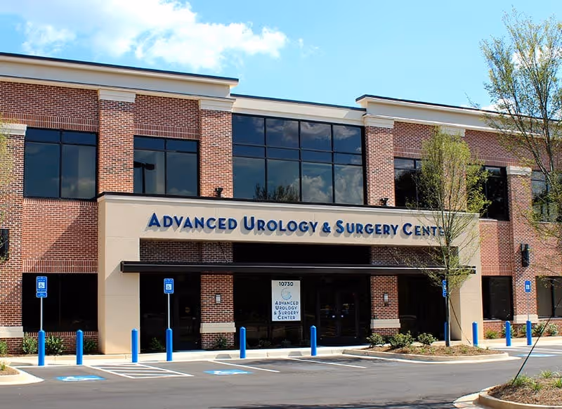 Brick medical center exterior with glass windows and a blue 'Advanced Urology & Surgery Center' sign.