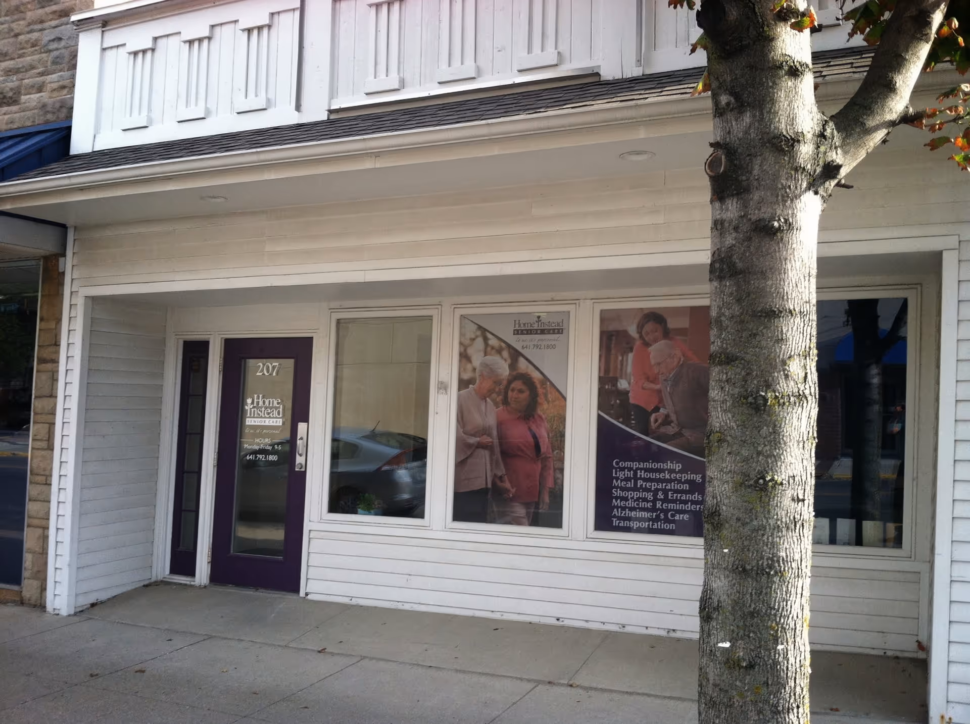 Storefront for Home Instead Senior Care with large posters in windows and a tree.