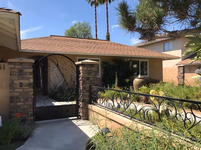 Front entrance to a beige single-story building with decorative wrought-iron gate and landscaping.
