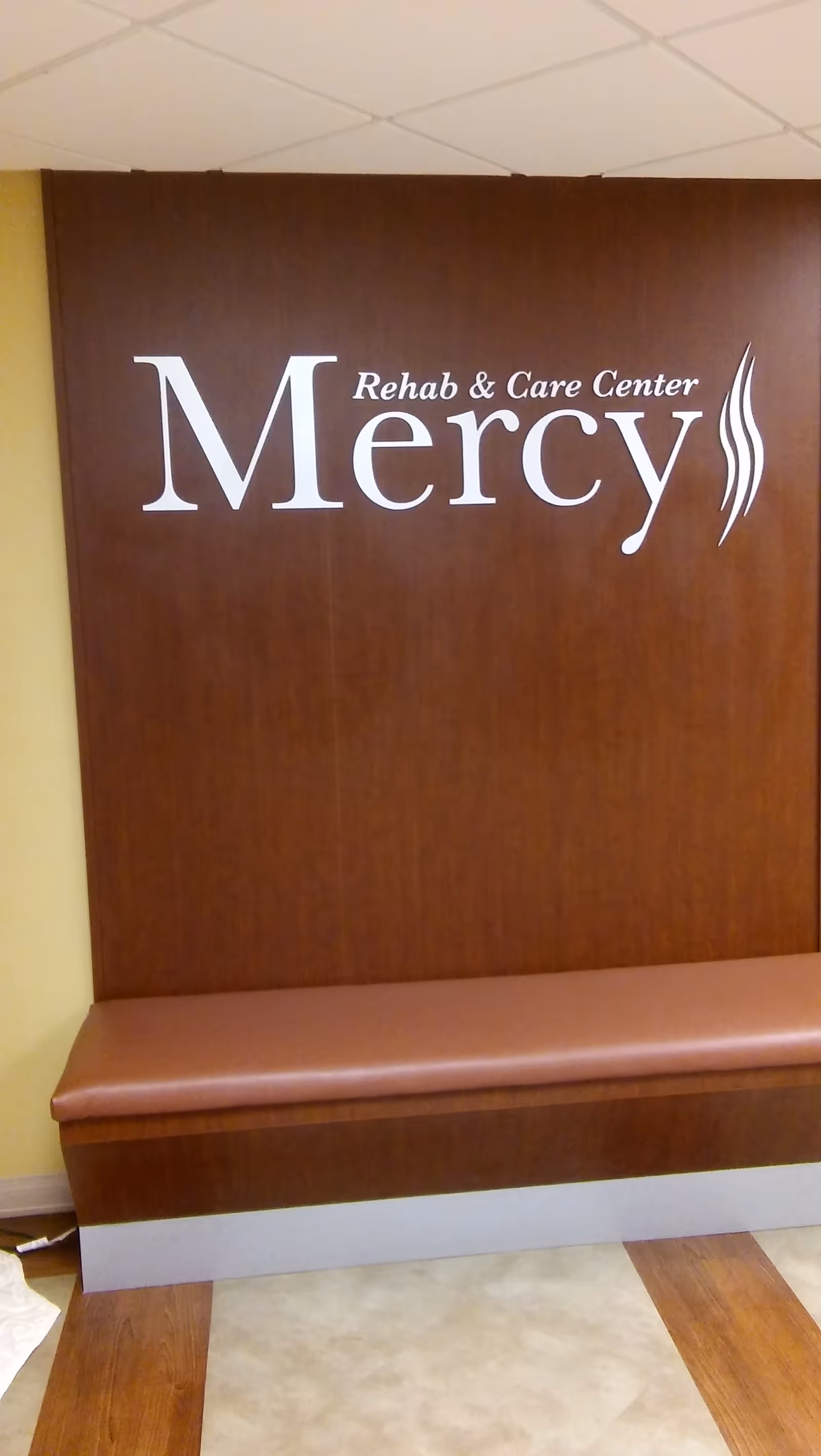 A wood-paneled wall with Mercy Rehab & Care Center sign and a brown bench.