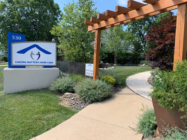 Entrance to Caring Matters Home Care with pathway, sign, wooden archway, and landscaping.