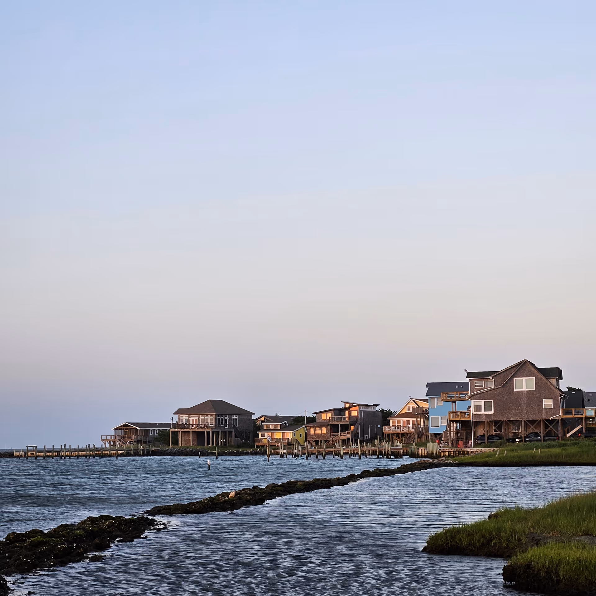 Row of colorful coastal houses on stilts beside calm water near the shore.