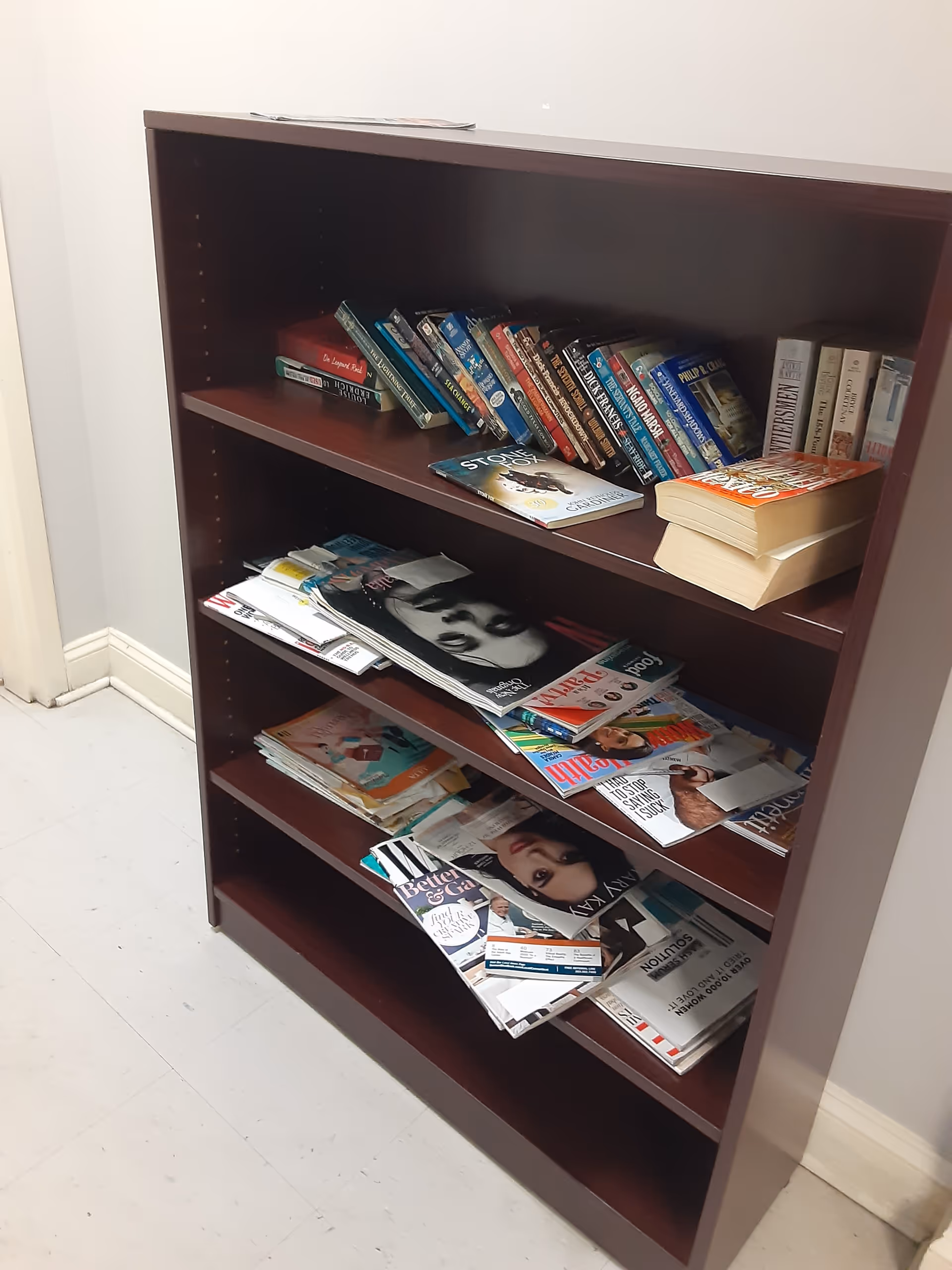 A wooden bookshelf filled with magazines and books in a hallway.