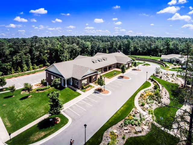 Aerial view of a senior living facility with parking, green lawns, and surrounding woods.