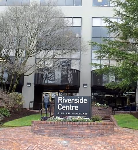 Front entrance of Riverside Centre building with sign, brick walkway, and trees.