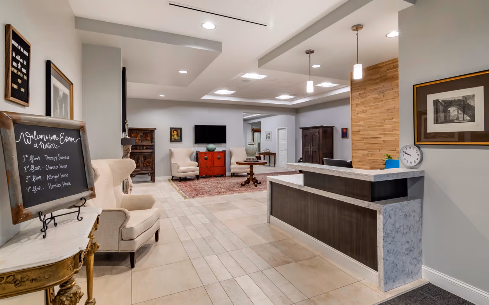 Reception lobby of a senior living facility with a front desk, seating area with armchairs, and a chalkboard welcome sign.