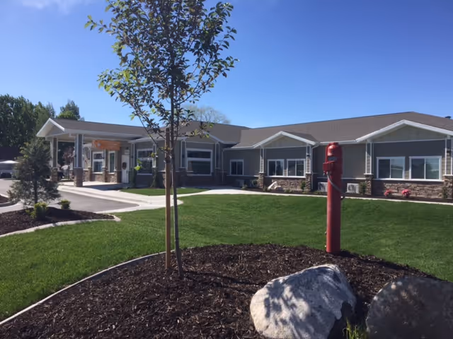 Exterior view of BeeHive Homes of Orem: single-story building with lawn, trees, and a red hydrant.