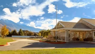 Front entrance of Hearthstone Manor with a covered porte-cochère, driveway, lawn, and mountains in the background.