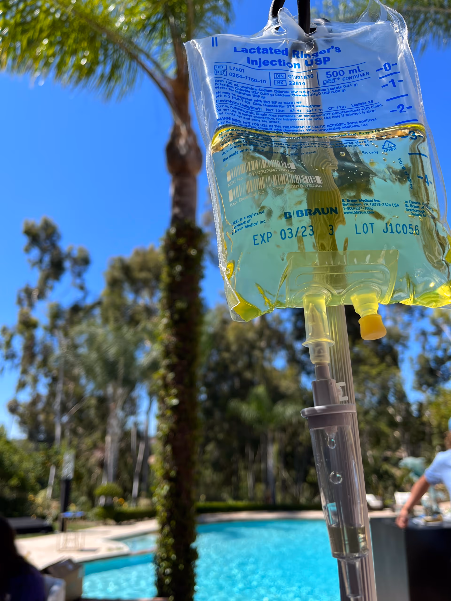 IV bag with yellow fluid outdoors near a pool