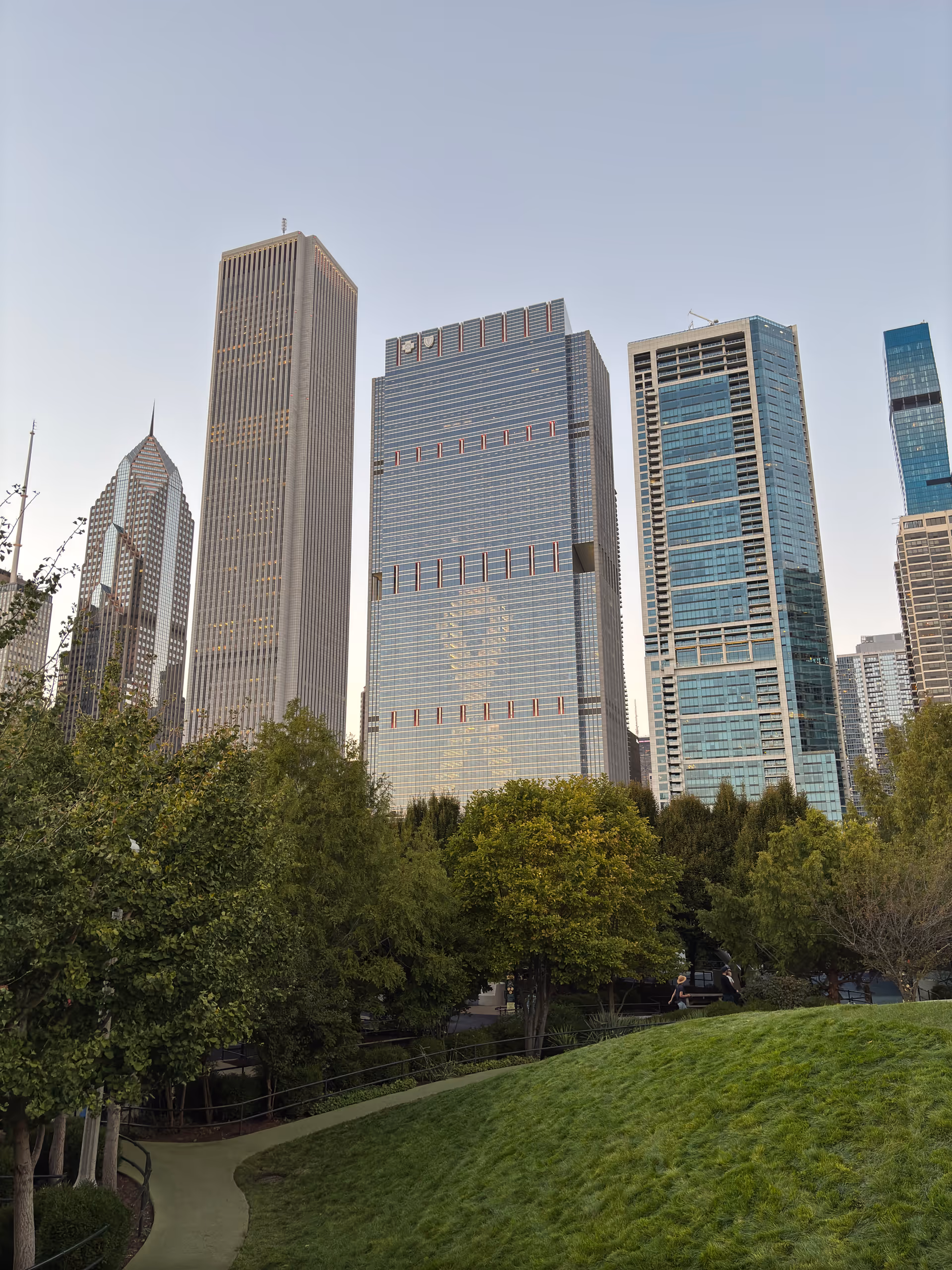 City skyline with tall glass buildings behind a grassy park and winding path.