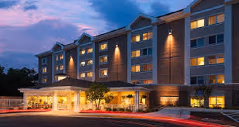 Tall Oaks Assisted Living exterior building at dusk with illuminated entrance and lit windows.