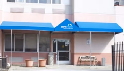 Front of Alaris Health at Hamilton Park with blue awnings, entrance, bench, planters.