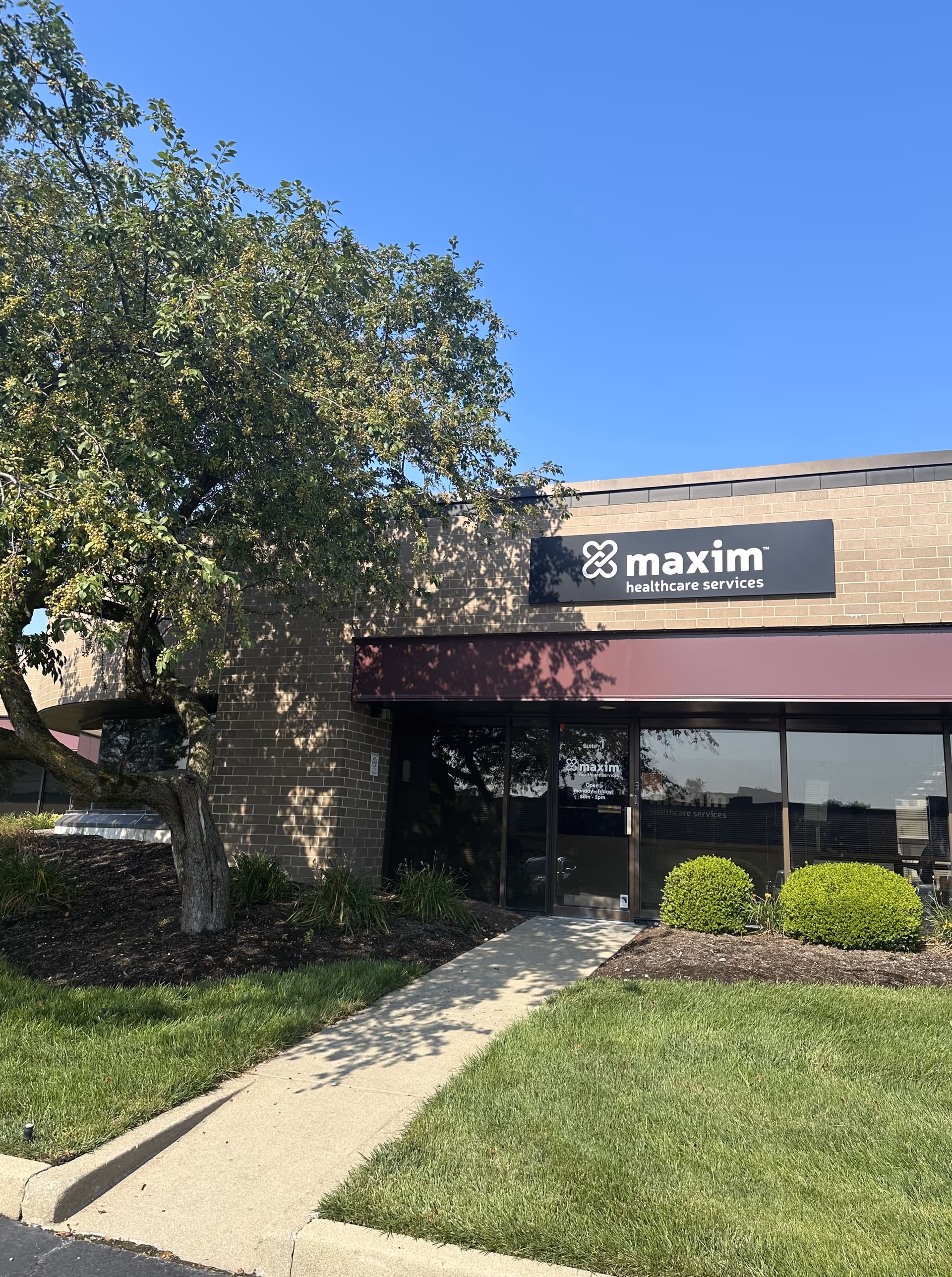 Exterior view of Maxim Healthcare Services building with glass doors and landscaping.