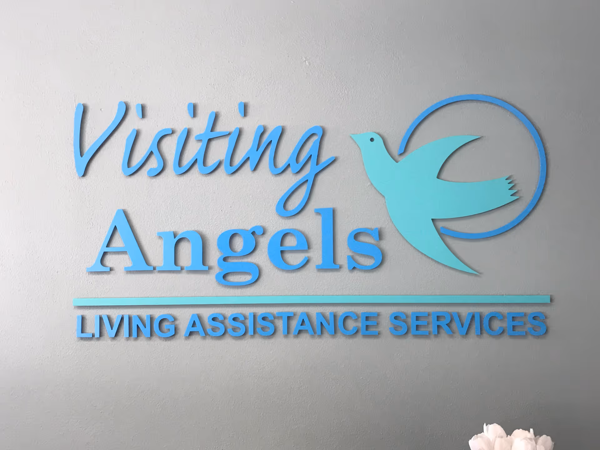 Interior wall sign showing Visiting Angels and teal dove logo on a gray background.