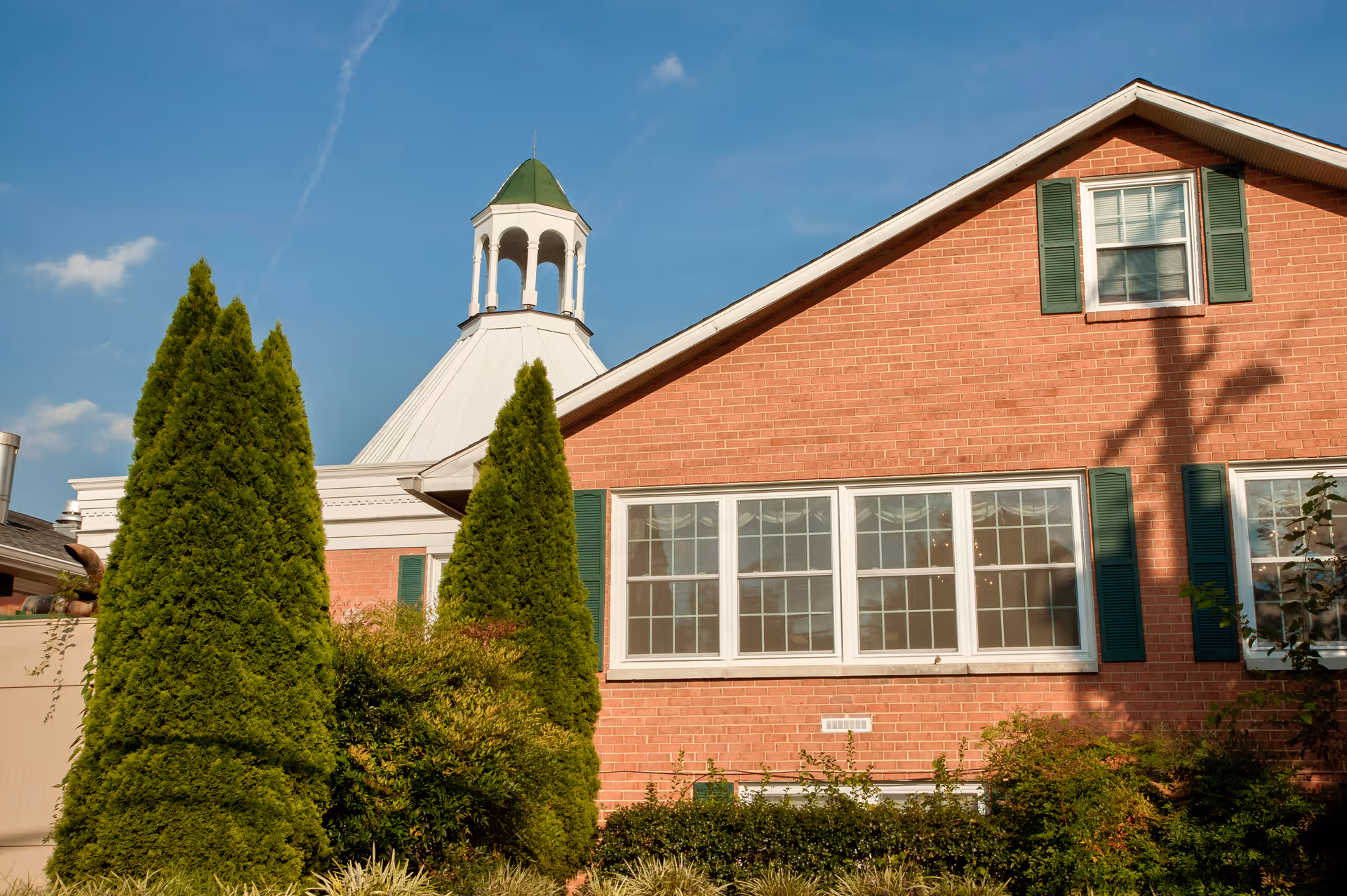 Brick exterior of Genesis Springbrook senior living facility with green shutters and a cupola.