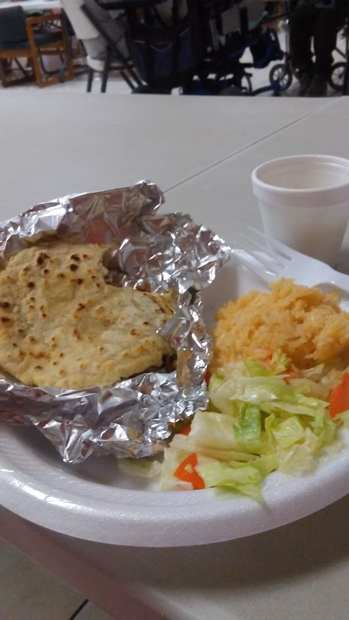 Foil wrapped bread, rice, and salad on a disposable plate in a dining area.