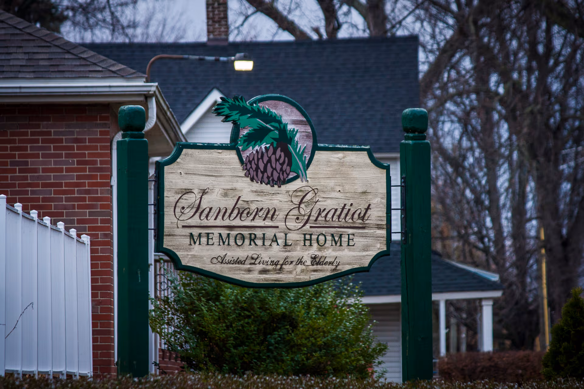 Front exterior sign for Sanborn Gratiot Memorial Home with brick building nearby.