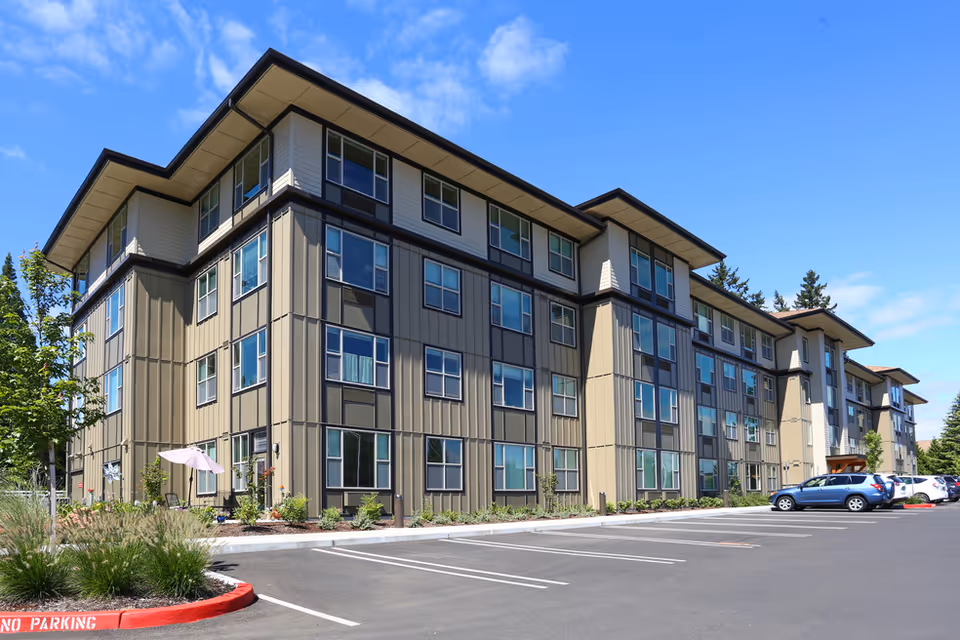 Modern three-story senior living building with large windows and a spacious parking lot.