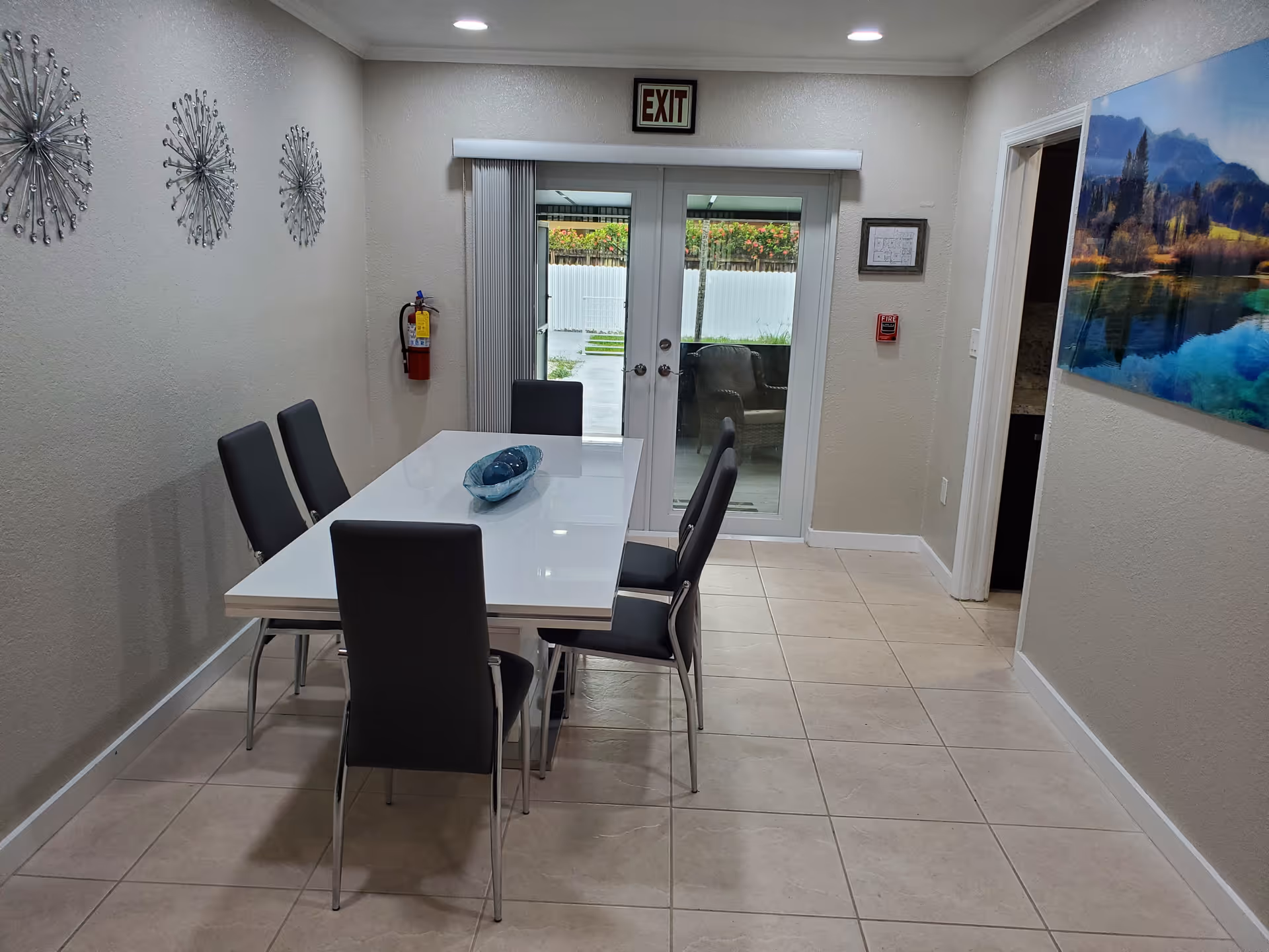 Modern dining room with a white table, six chairs, and exterior glass doors.