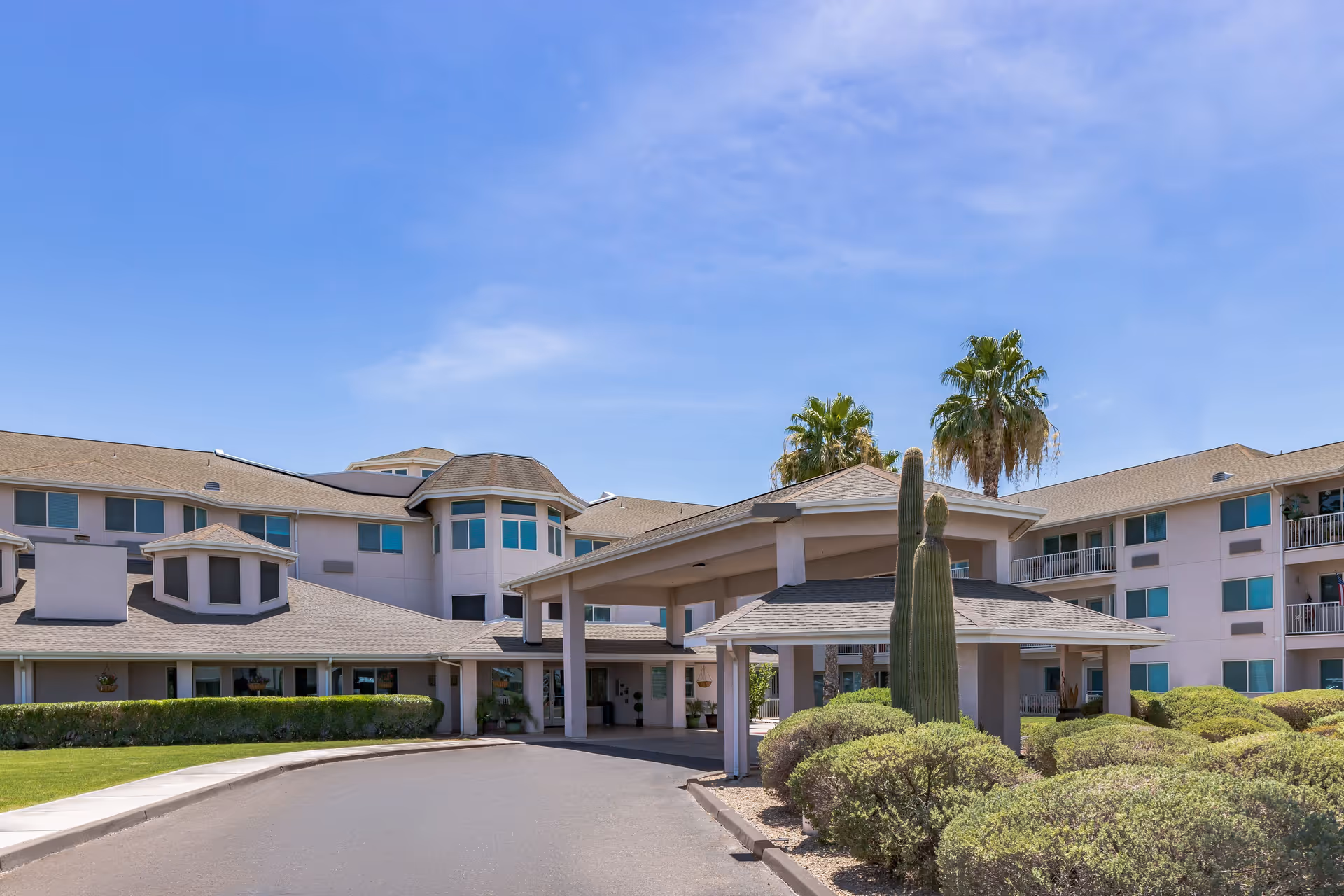 Exterior front entrance of a multi-story senior living building with a porte-cochère, palm trees, and desert landscaping.