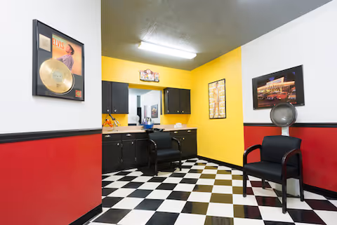 Interior salon area with checkered floor, black chairs, and yellow and red walls.