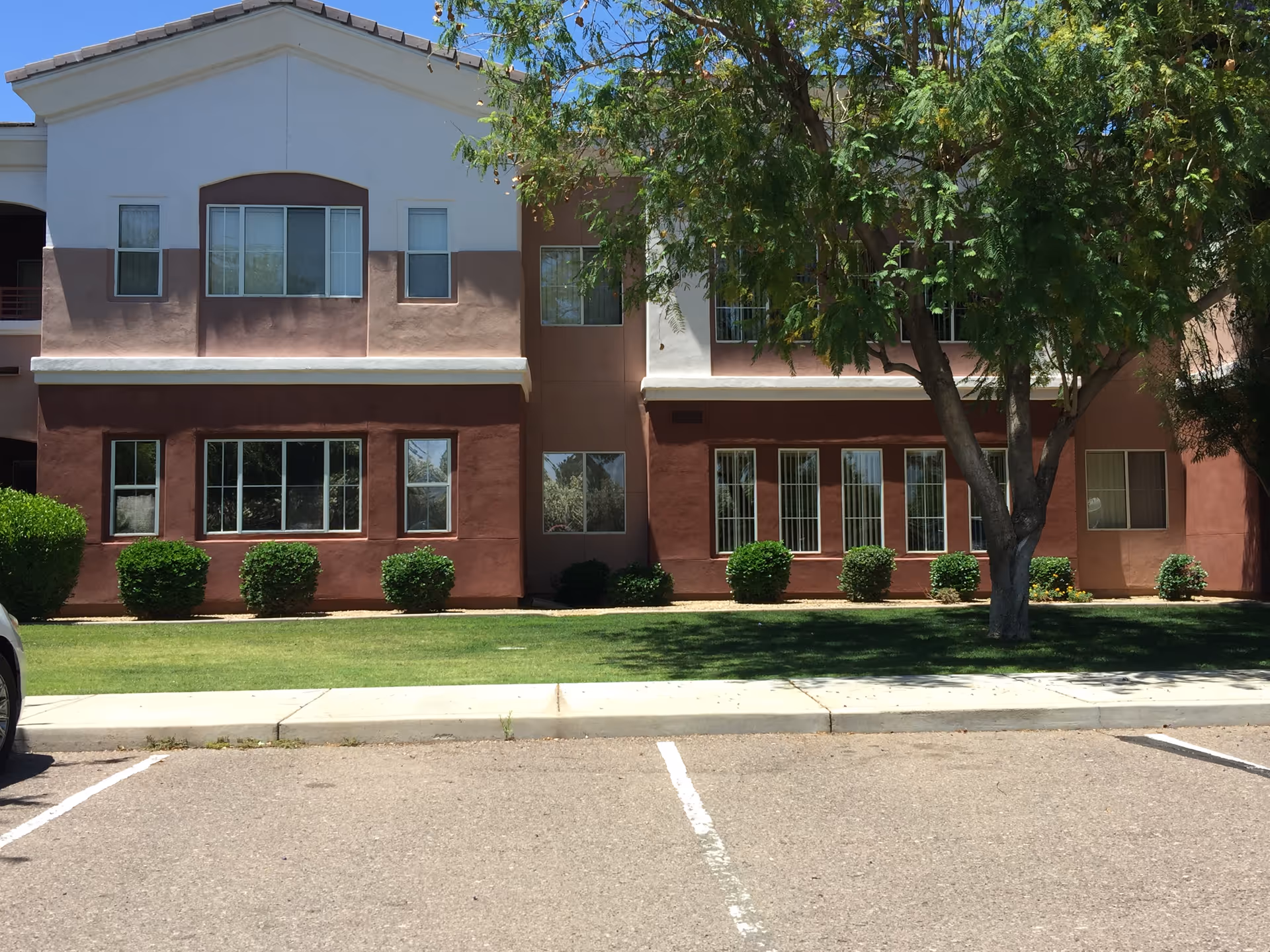 Exterior view of a two-story assisted living building with windows, trees, and parking.