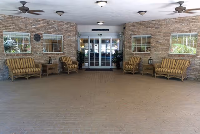 Covered entrance area with wicker seating and glass double doors leading into the building.