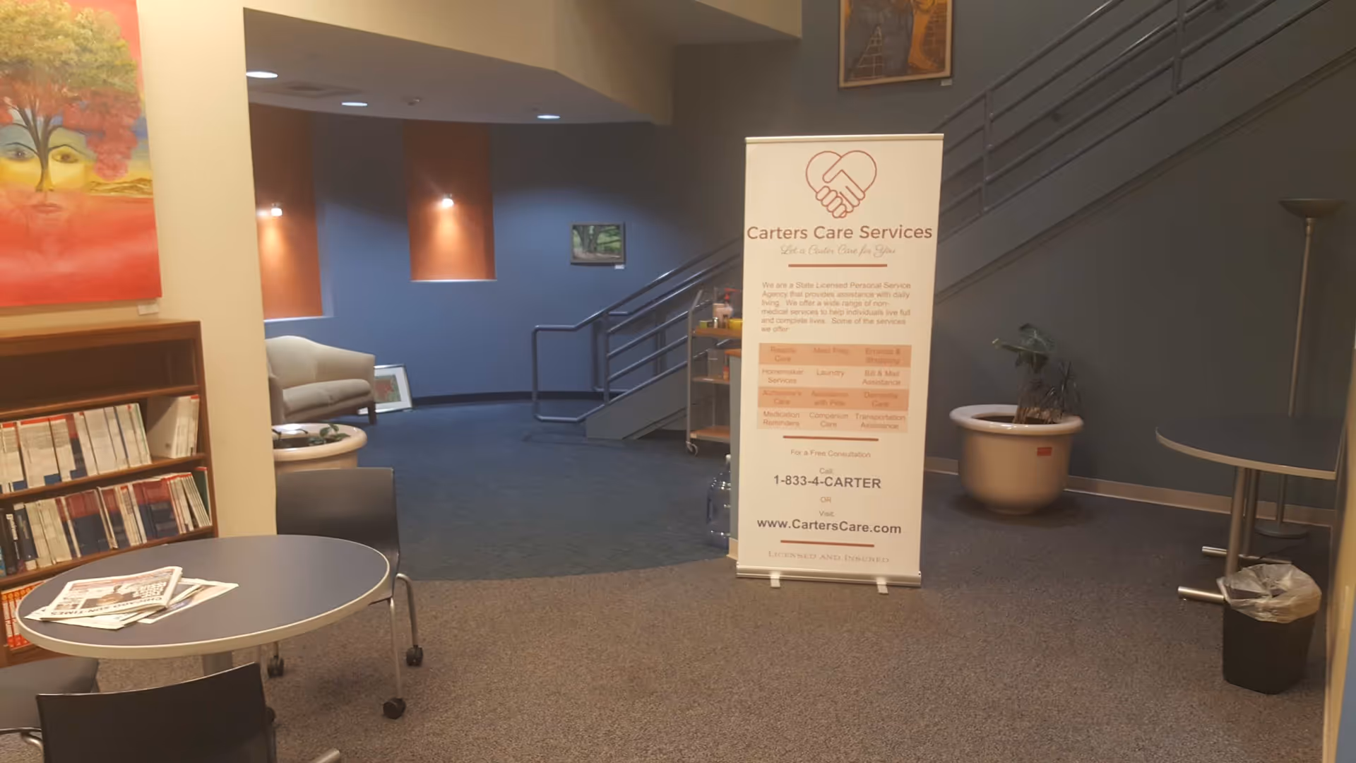 Interior lobby featuring Carters Care Services banner, seating, stairs, a bookshelf, and tables.