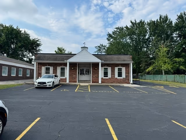 Front view of a brick senior care facility with a small entrance and parking lot.